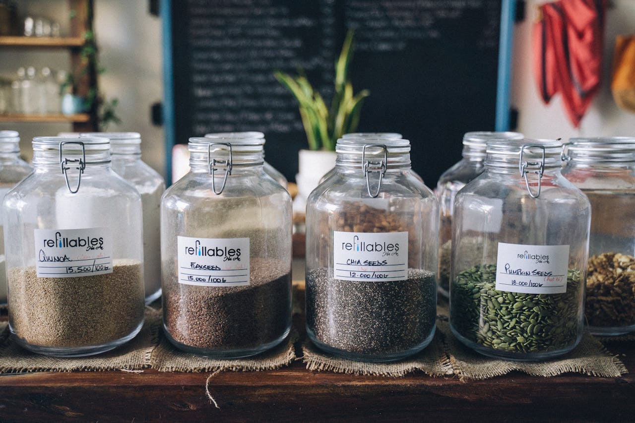 about-05 Glass jars in a store containing organic seeds like quinoa and flax, promoting sustainable living.